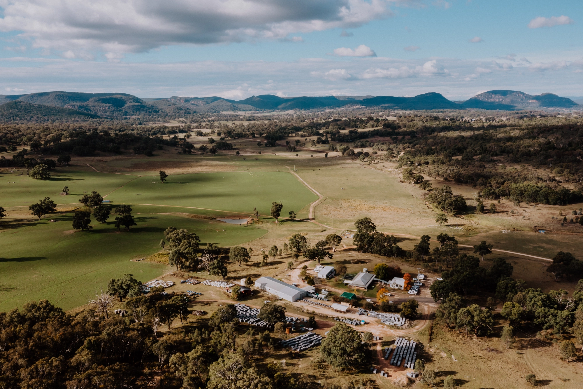 Aerial view of a rural landscape, including Bowdens Silver, with scattered buildings, open fields, clusters of trees, and distant hills under a partly cloudy sky.